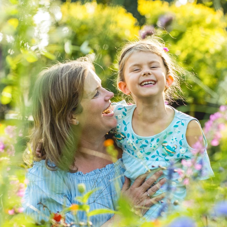 Mutter und Tochter im Blumenfeld Frau hält ihr Kind im Arm inmitten von bunten Blumen bei warmem Sonnenlicht.