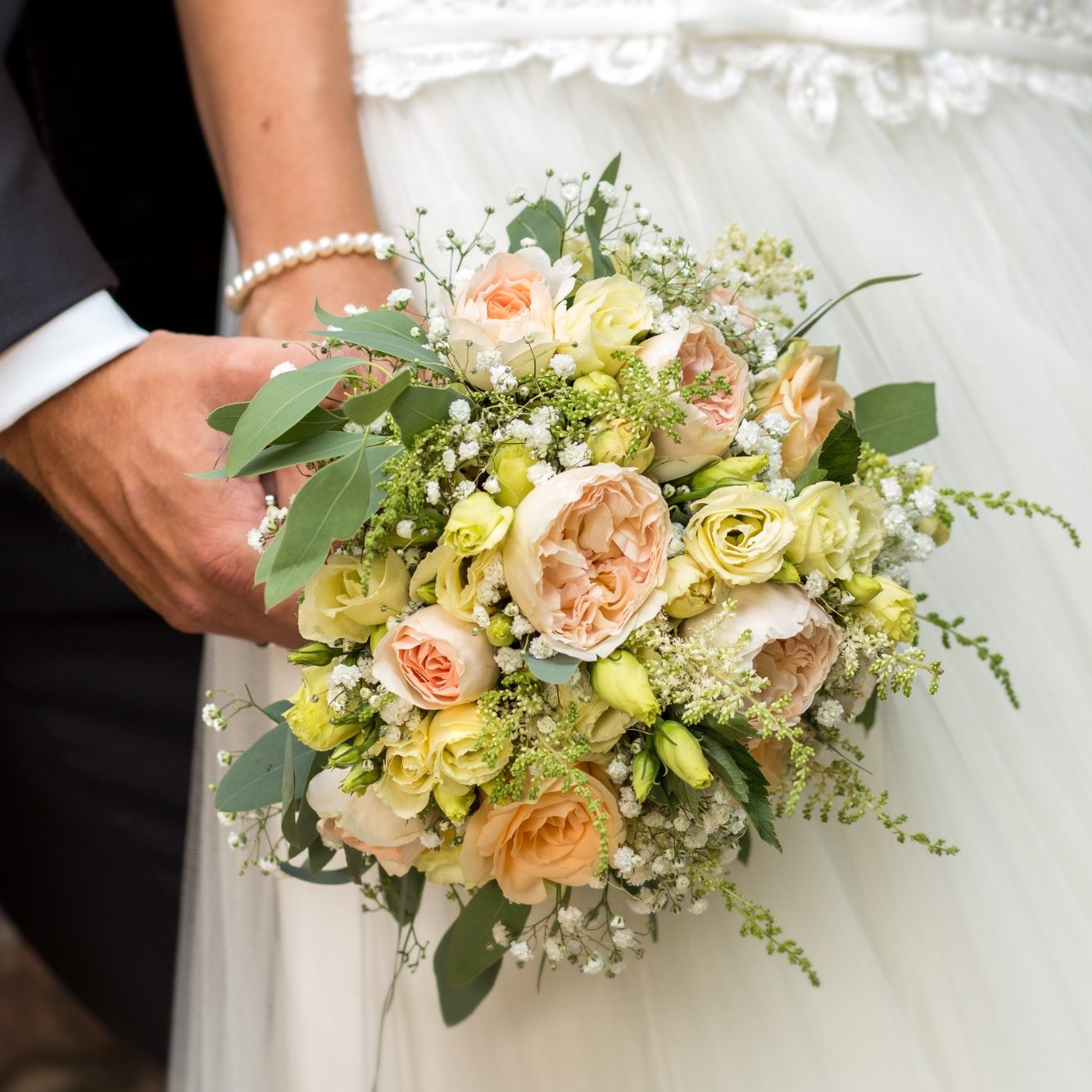 Brautstrauß vor Hochzeitskleid Brautpaar hält einen Blumenstrauß aus Rosen und Grün vor dem Hochzeitskleid.