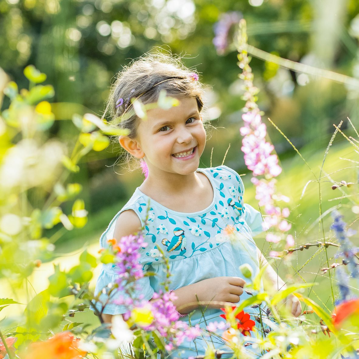 Mädchenportrait im Blumenfeld Lächelndes Mädchen steht zwischen bunten Blumen bei natürlichem Tageslicht.
