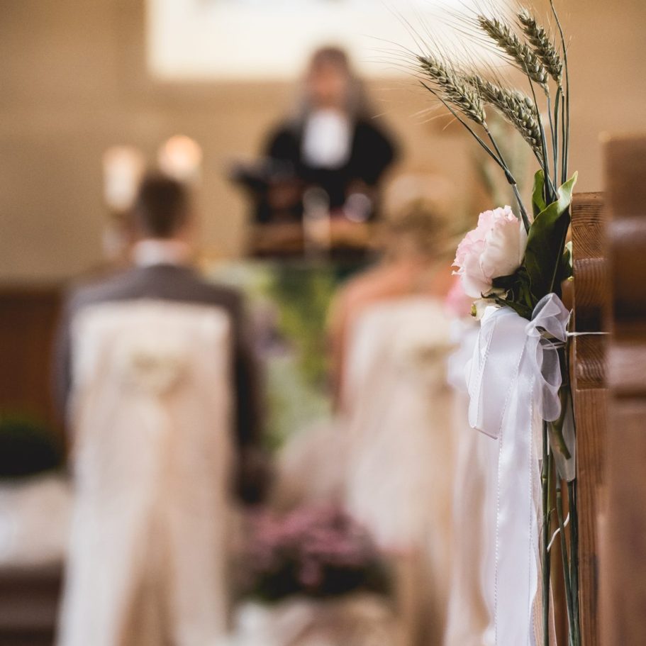 Kirchliche Trauung mit Blumenschmuck Blumengesteck mit Schleife an Kirchenbank während der Trauung.