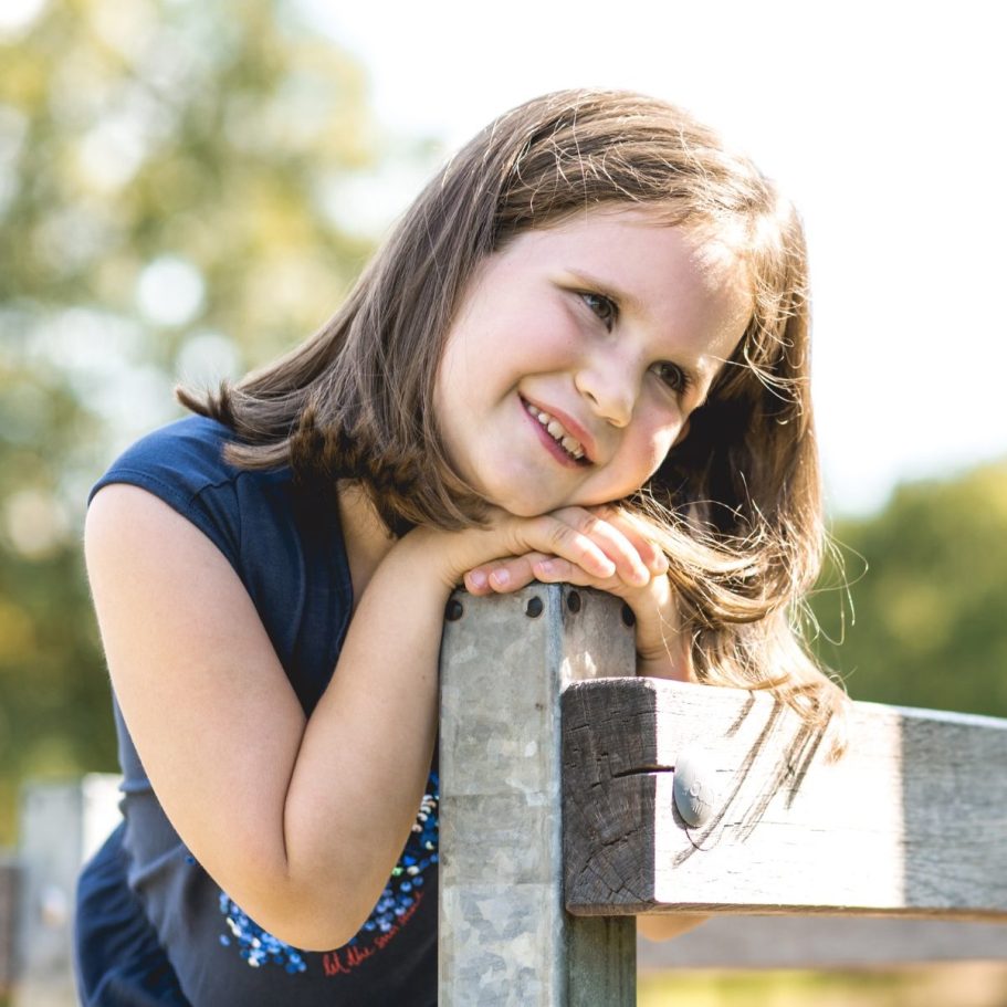 Portrait eines Mädchens im Freien Mädchen lehnt an einer Holzbank und lächelt bei natürlichem Sonnenlicht im Park.