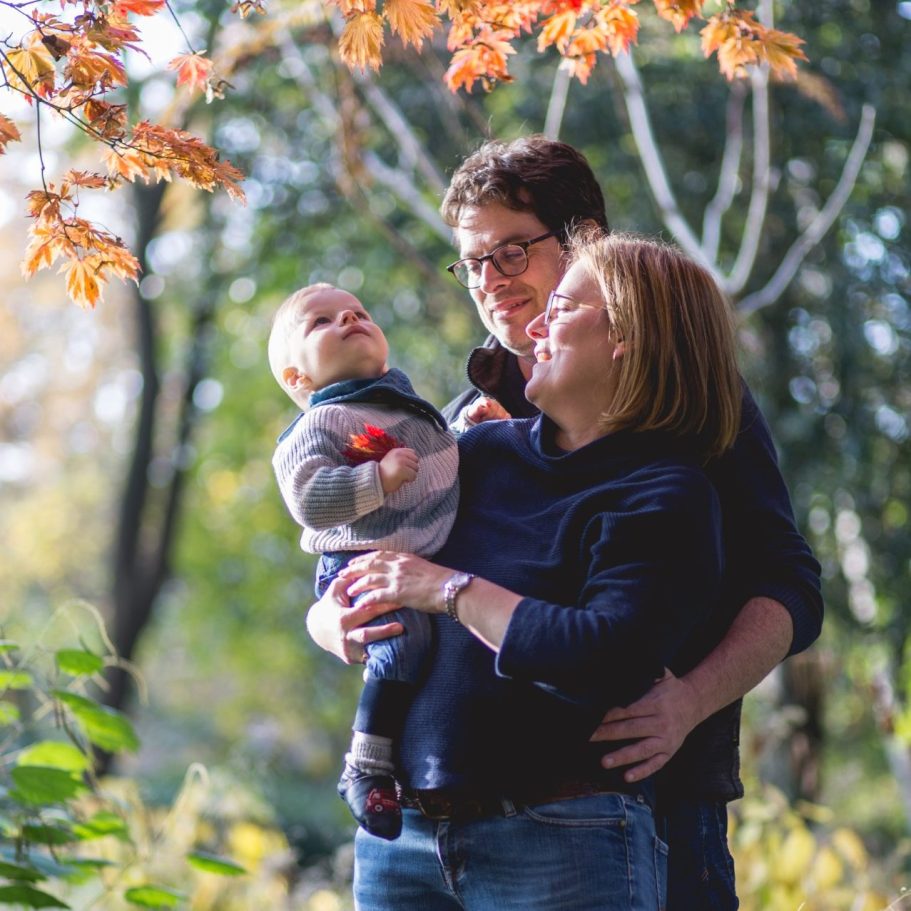 Familienportrait mit Baby im Herbst Eltern halten ihr Baby unter bunten Herbstblättern bei natürlichem Tageslicht im Park.