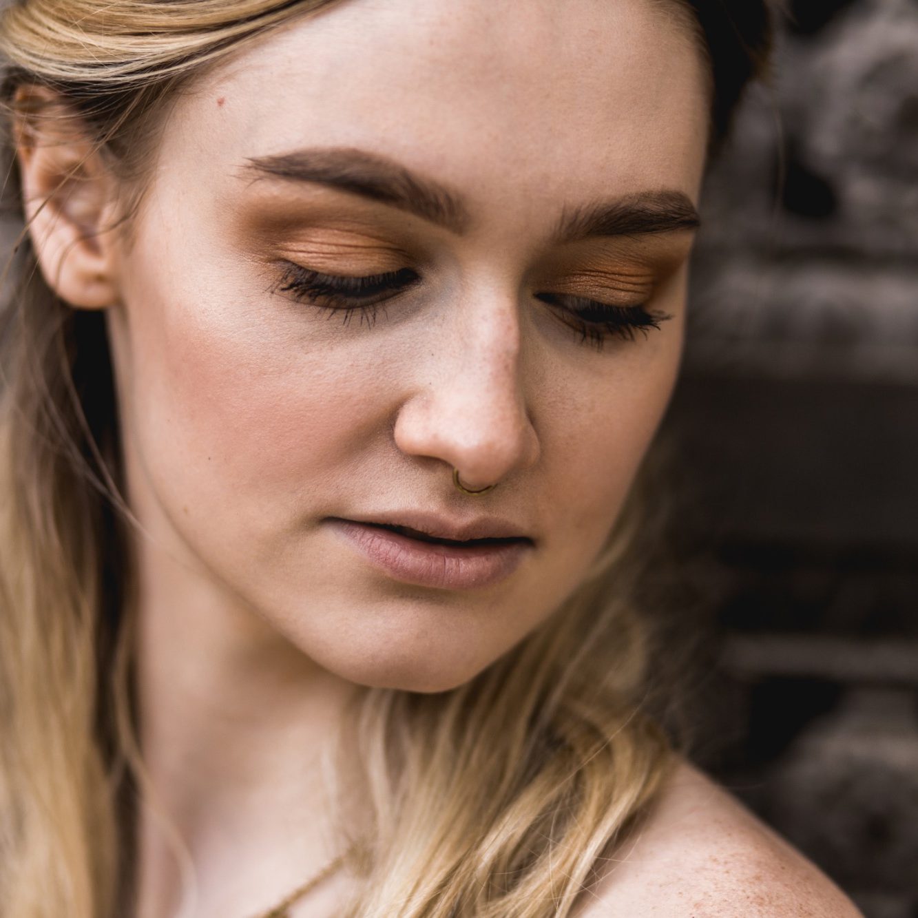 Nahportrait einer Frau vor dunklem Hintergrund Nahaufnahme einer jungen Frau mit gesenktem Blick vor dunklem, strukturiertem Hintergrund.