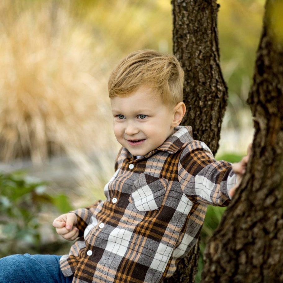 Jungenportrait im Park Kleiner Junge lehnt an einem Baum und lächelt bei einem Outdoor-Fotoshooting im Grünen.