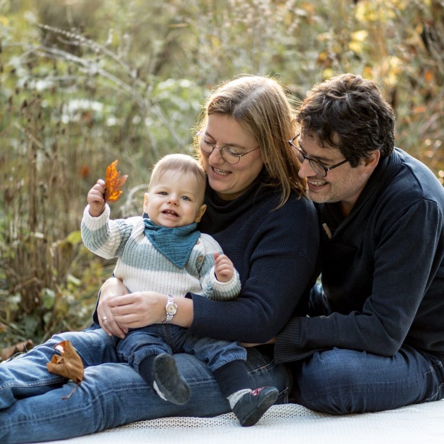 Familienportrait mit Baby im Sitzen Eltern sitzen mit ihrem Baby auf einer Decke in herbstlicher Naturumgebung.