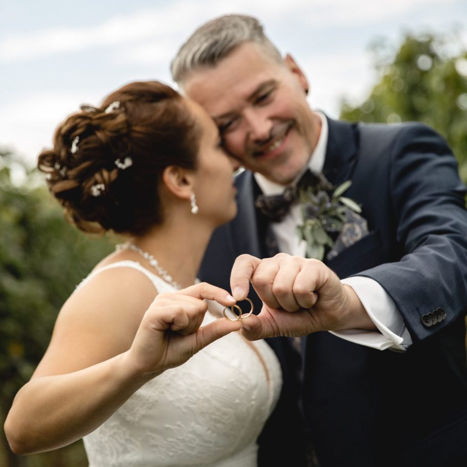 Brautpaar zeigt Eheringe Hochzeitspaar präsentiert Eheringe im Weinberg.