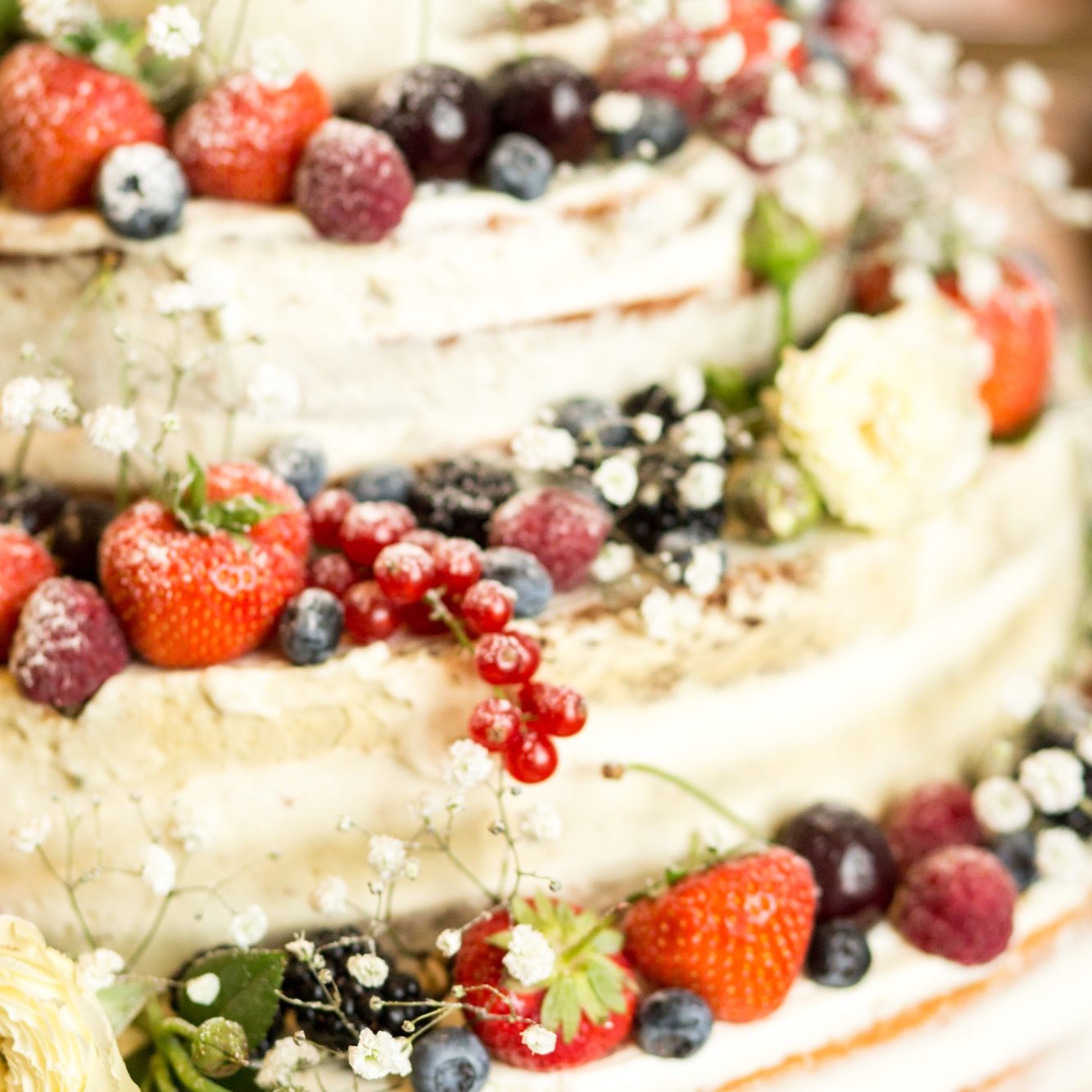 Hochzeitstorte mit Beeren und Blumen Mehrstöckige Hochzeitstorte mit frischen Beeren, Blumen und Cremefüllung in Nahaufnahme.
