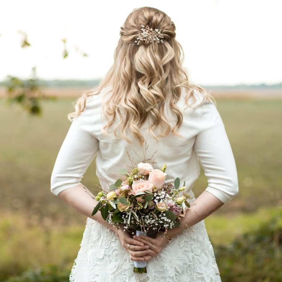 Braut mit Blumenstrauß von hinten Rückansicht der Braut mit Blumenstrauß vor einer weiten Landschaft.