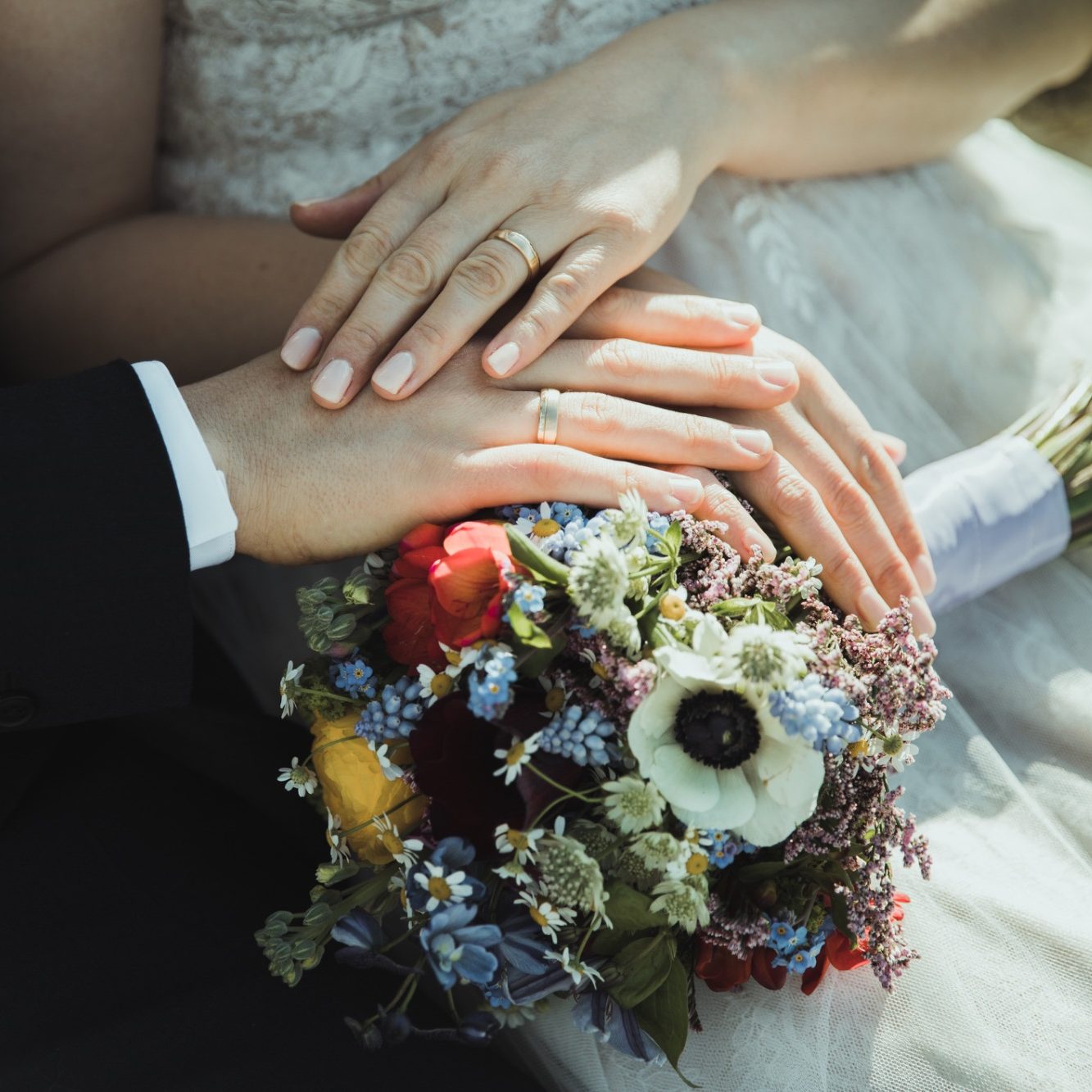 Hochzeitsringe und Brautstrauß Hände von Braut und Bräutigam liegen auf einem bunten Brautstrauß.