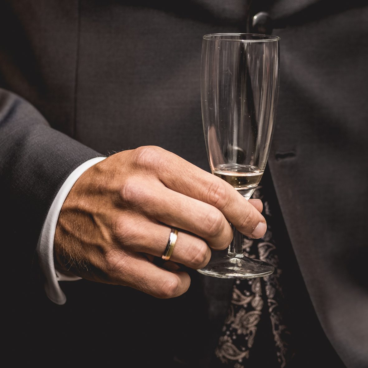 Bräutigam hält Sektglas bei der Hochzeit Hand des Bräutigams mit Ehering hält ein Sektglas beim Hochzeitsempfang.