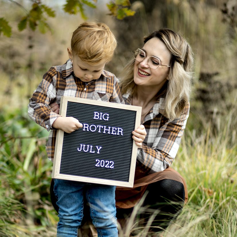 Mutter mit Kind und Tafel im Freien Frau und Kleinkind halten eine beschriftete Tafel bei einem Familien-Fotoshooting in der Natur.
