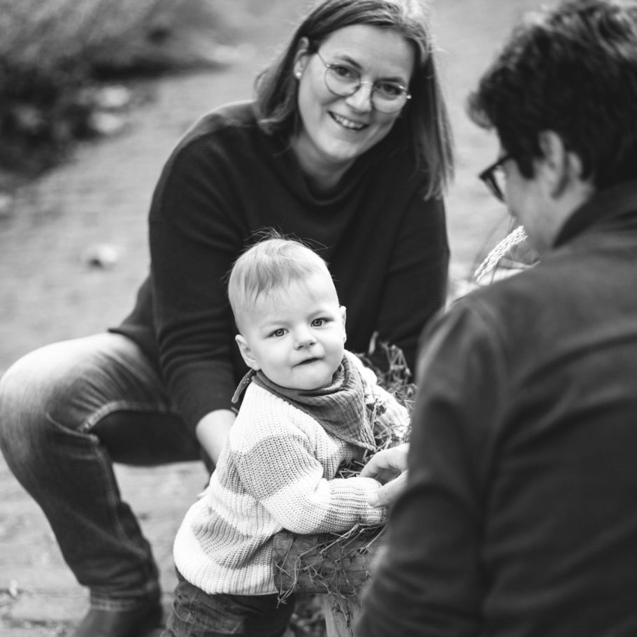 Schwarzweiß Familienportrait mit Baby Eltern und Baby in entspannter Pose auf einem Weg im Freien, fotografiert in Schwarzweiß.