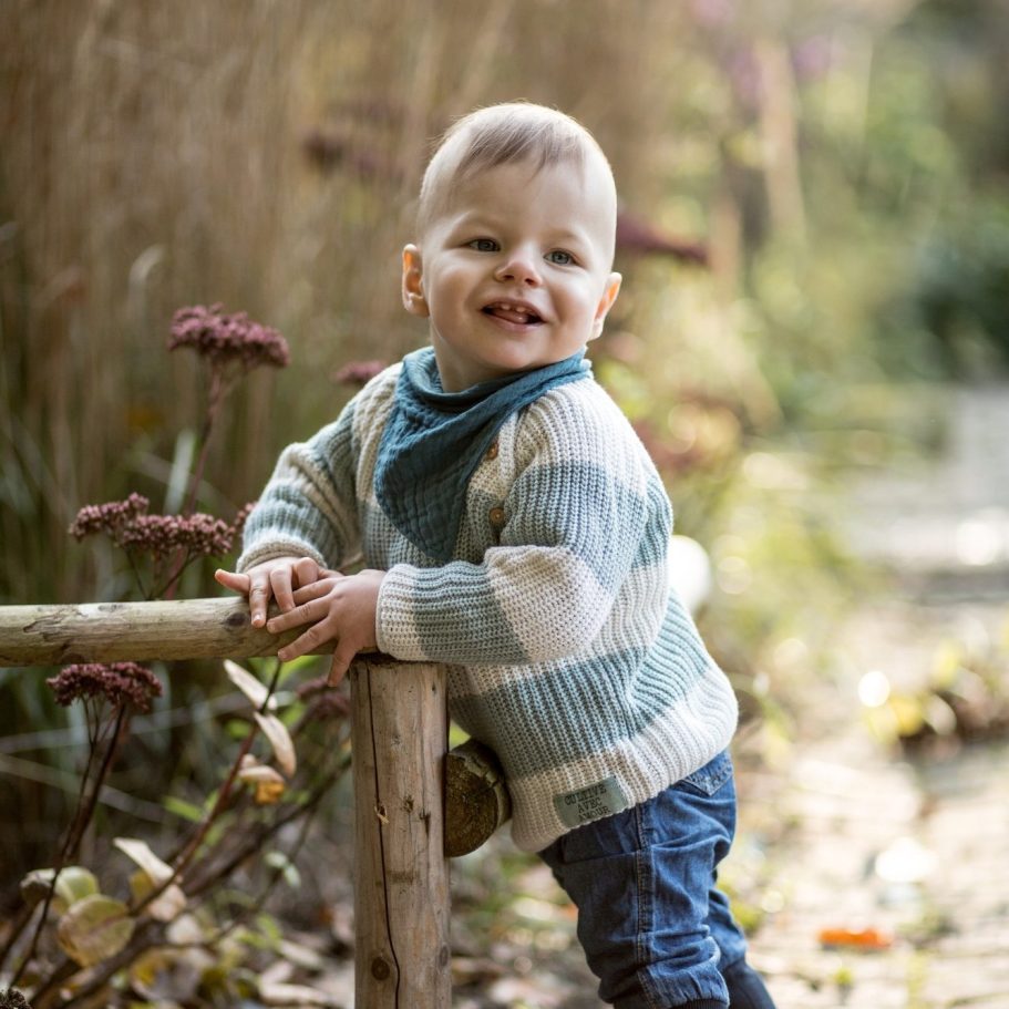 Schwarzweiß Baby Portrait im Freien Kleinkind lehnt an einem Holzgeländer auf einem Weg in natürlicher Umgebung bei weichem Tageslicht, fotografiert in Schwarzweiß.