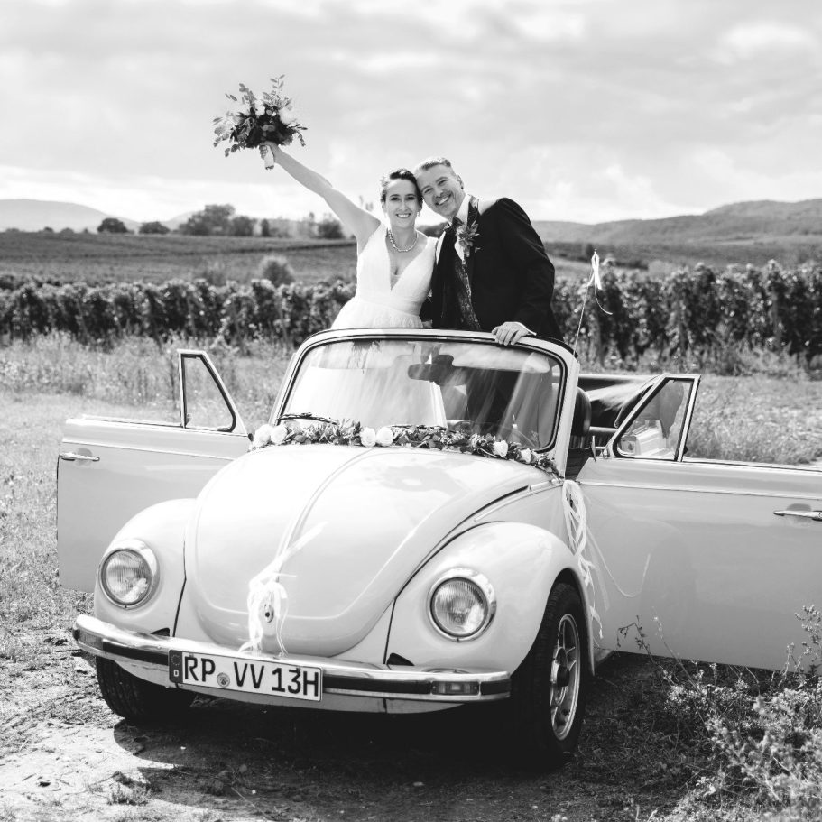 Brautpaar im Oldtimer Cabrio Brautpaar feiert Hochzeit im offenen Oldtimer, fotografiert in Schwarzweiß.