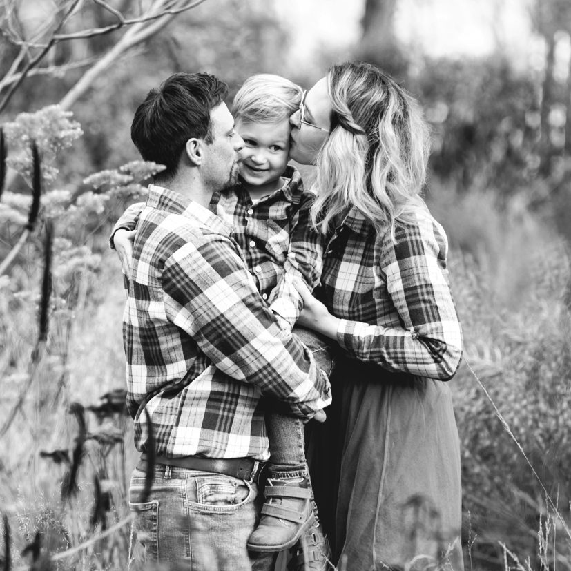 Schwarzweiß Familienportrait mit Kind Eltern halten ihr Kind im Arm und geben ihm einen Kuss bei einem Outdoor-Fotoshooting.