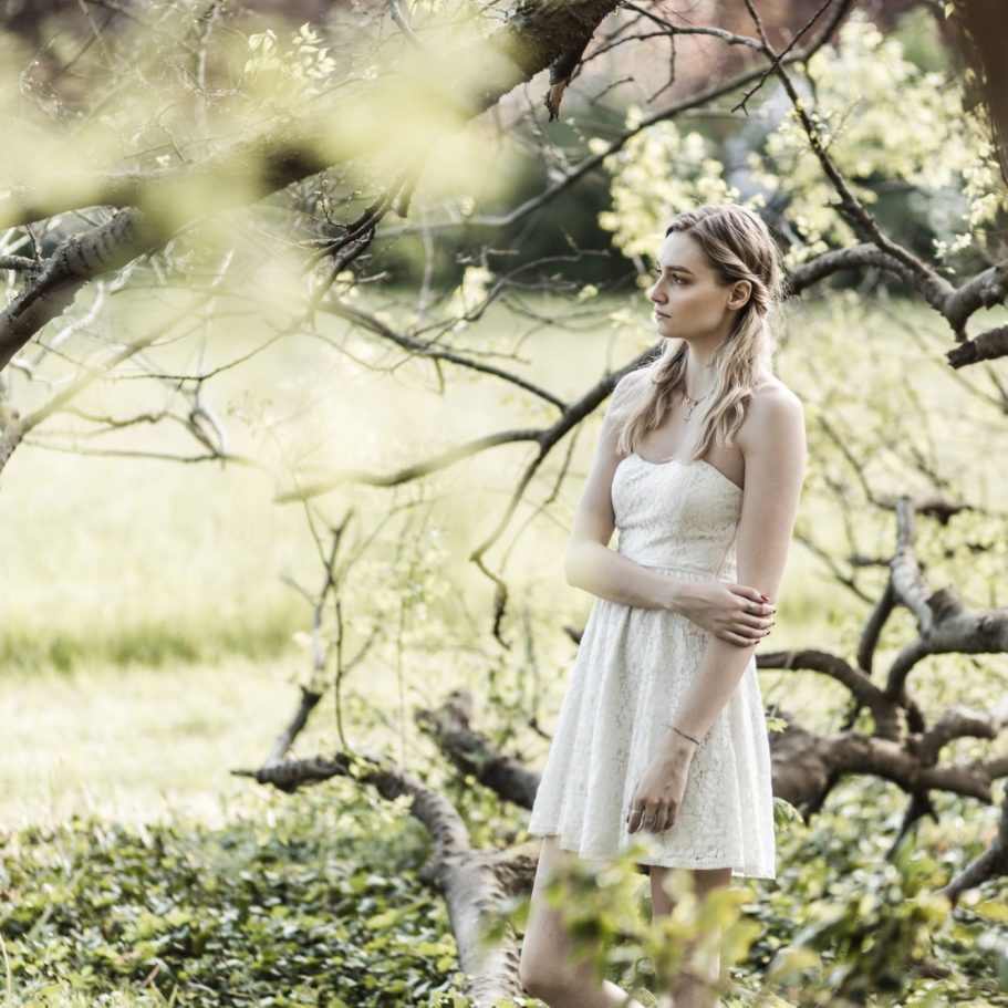 Ganzkörperportrait einer Frau im weißen Kleid im Wald Frau in hellem Kleid zwischen Bäumen in natürlicher Umgebung bei sanftem Licht.