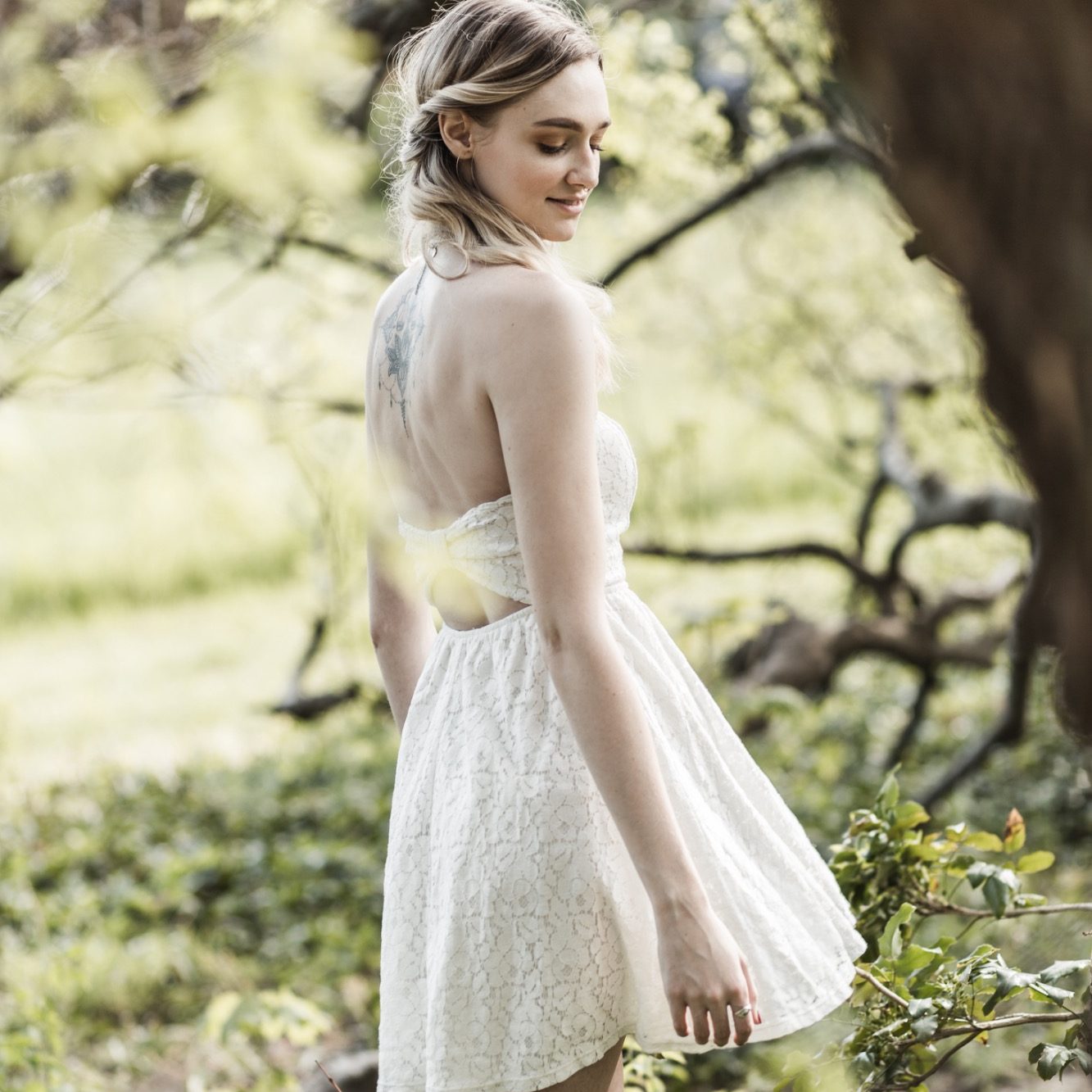 Rückenansicht einer Frau im weißen Kleid Frau im hellen Kleid von hinten fotografiert in grüner Outdoor-Umgebung.