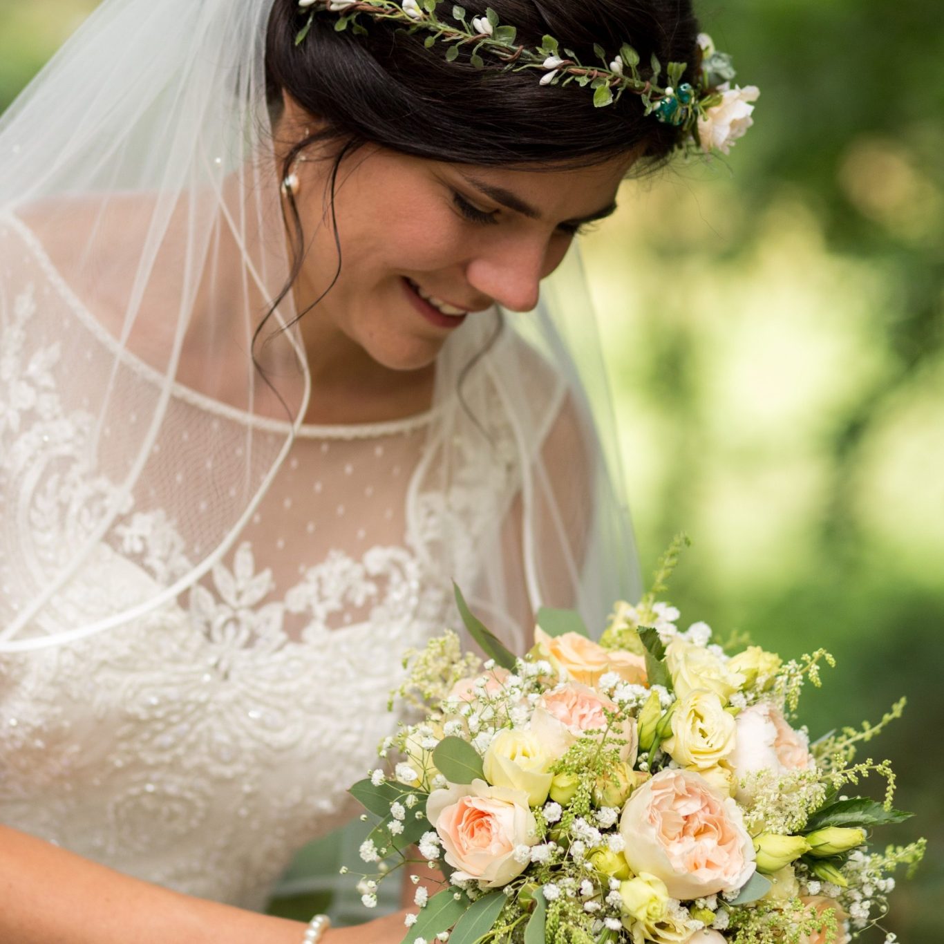Braut mit Blumenkranz und Brautstrauß Braut blickt lächelnd auf ihren Blumenstrauß in natürlicher Umgebung.