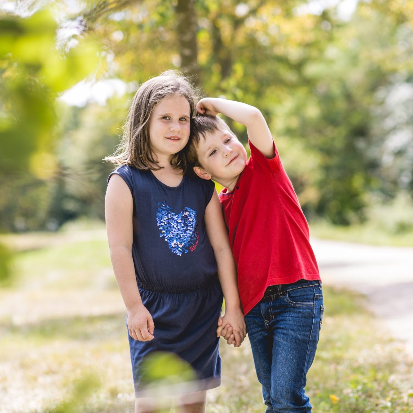 Kinderportrait im Park Zwei Kinder stehen auf einem Weg im Grünen und halten sich an den Händen.